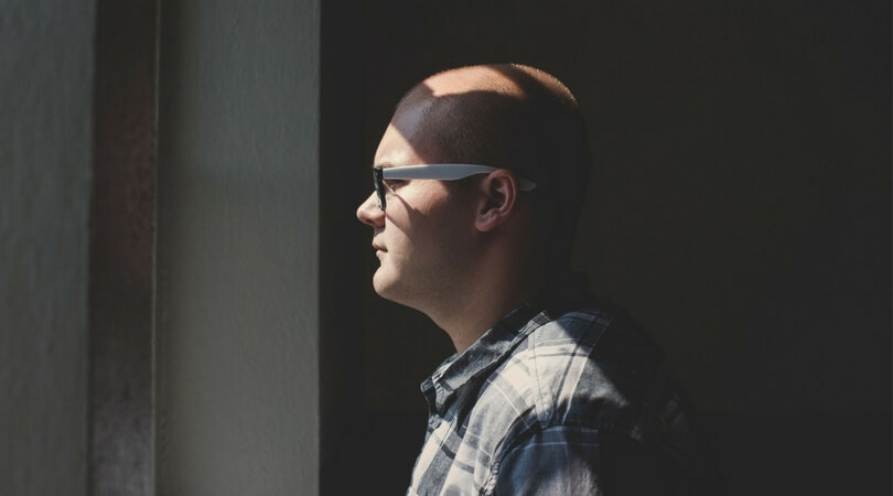 Man wearing eyeglasses standing in the dark and looking out a window